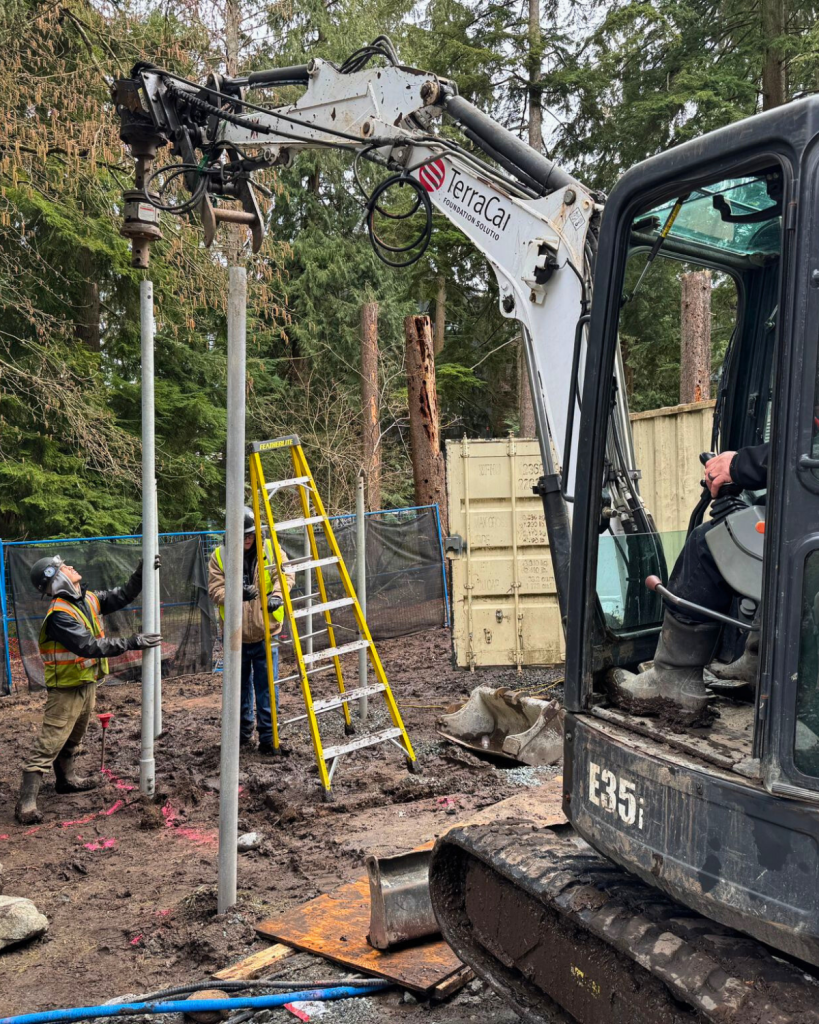 TerraCana crew member installing a helical pile using an E35 mini excavator in a densely wooded environmentally sensitive area at Woodland Park, Port Moody BC