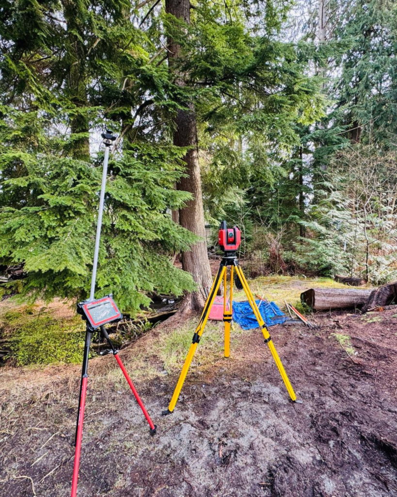 Surveyor's equipment including a yellow tripod and survey rod set up in a forested area during site preparation