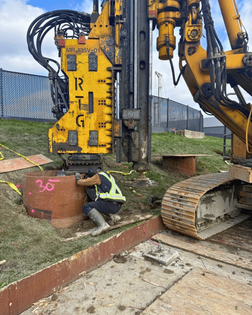 Close-up of yellow RG branded drilling rig head with hydraulic attachments during caisson installation at the Langley Events Centre